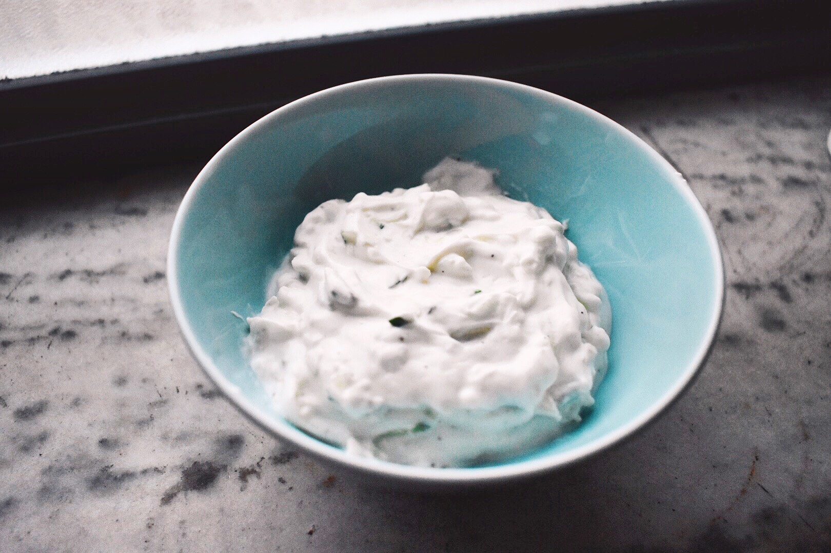 Tzaziki sauce in a blue bowl on a marble background