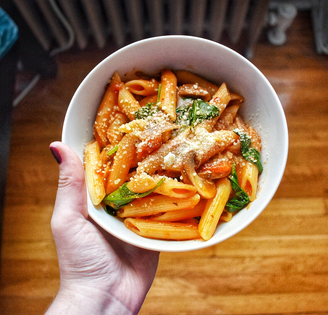 Penne Pasta in a white bowl with red sauce, parmesan cheese, spinach, onion, and mushroom