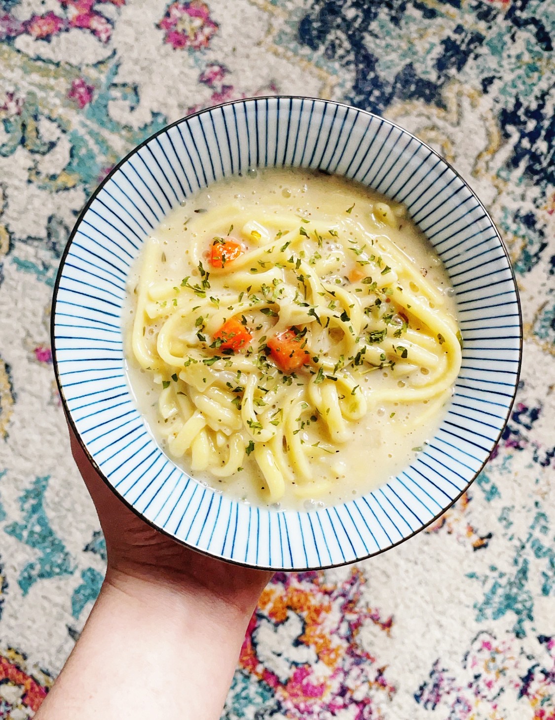 striped blue and white bowl with creamy broth, carrot, and noodles.