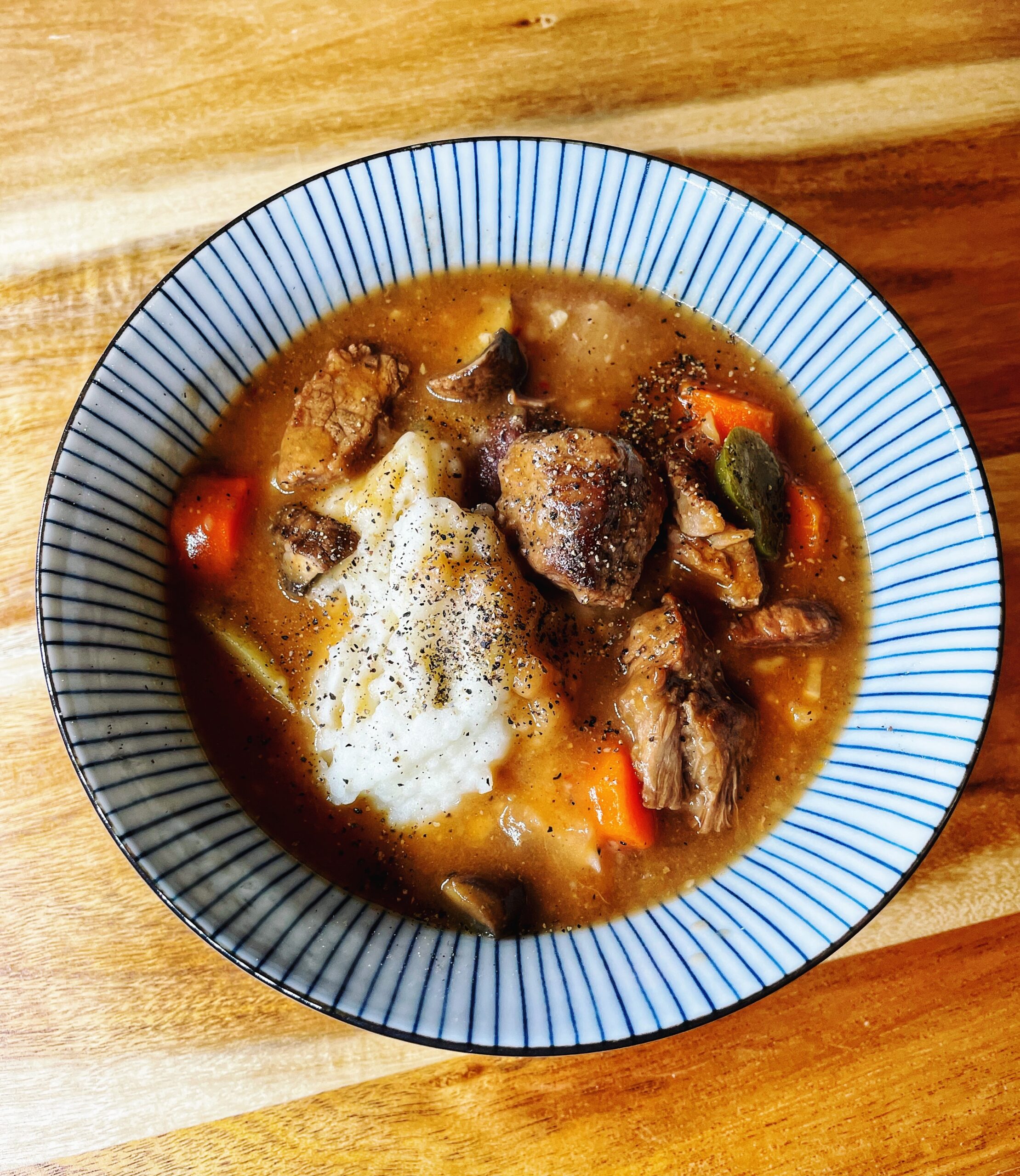 Irish beef stew with beef, potatoes, carrots, and jalapeno in a blue and white bowl on a wood board.