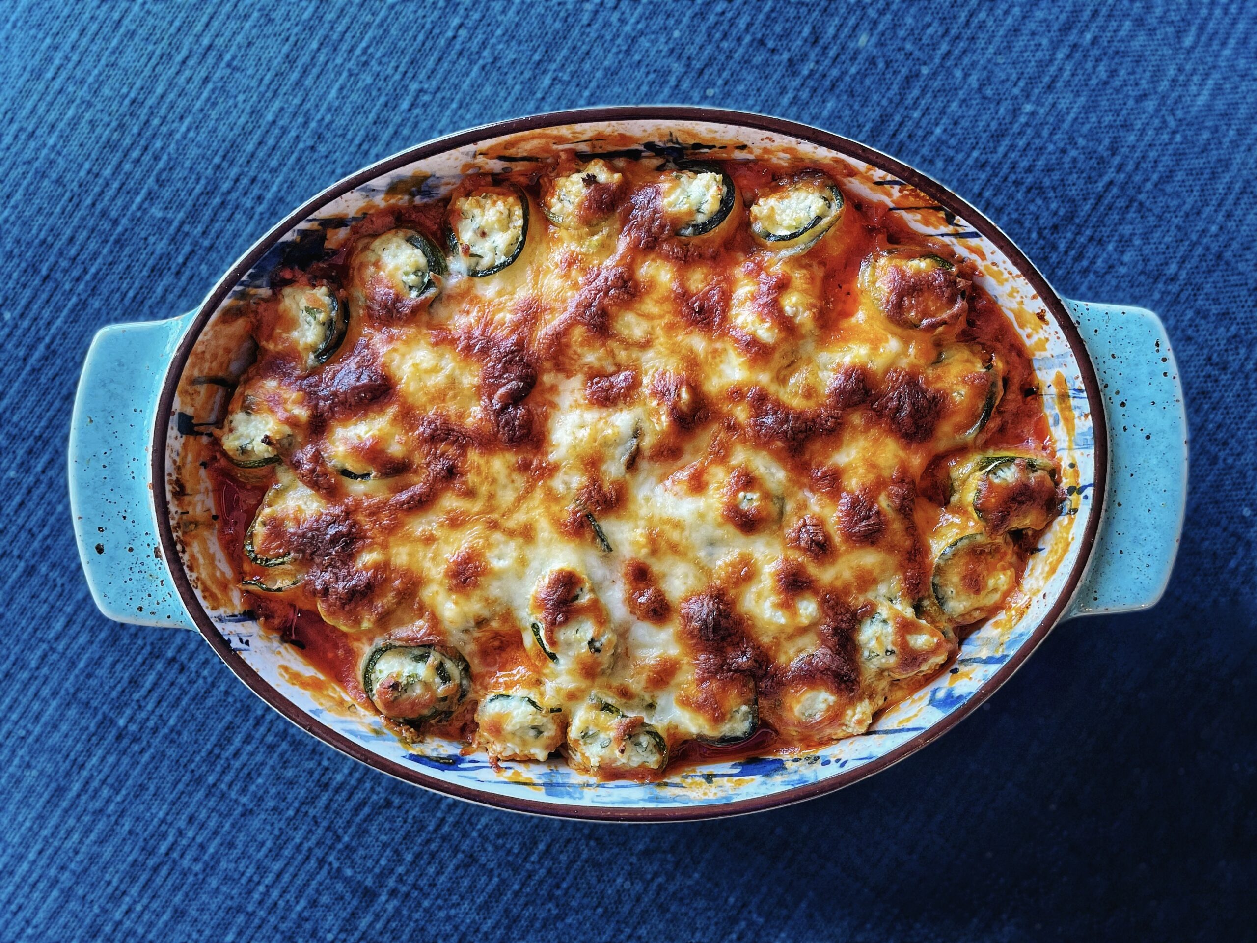 casserole dish with stuffed, rolled zucchini covered in cheese with a layer of marinara sauce