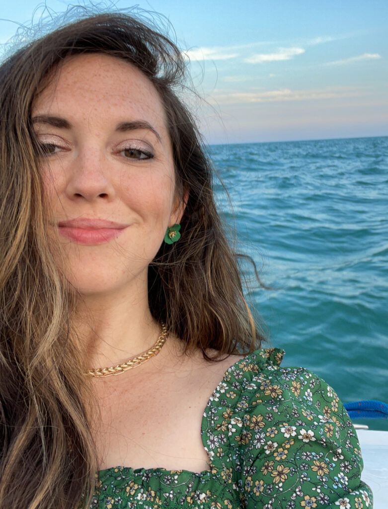 Woman with long brown hair and a green shirt with water in the background